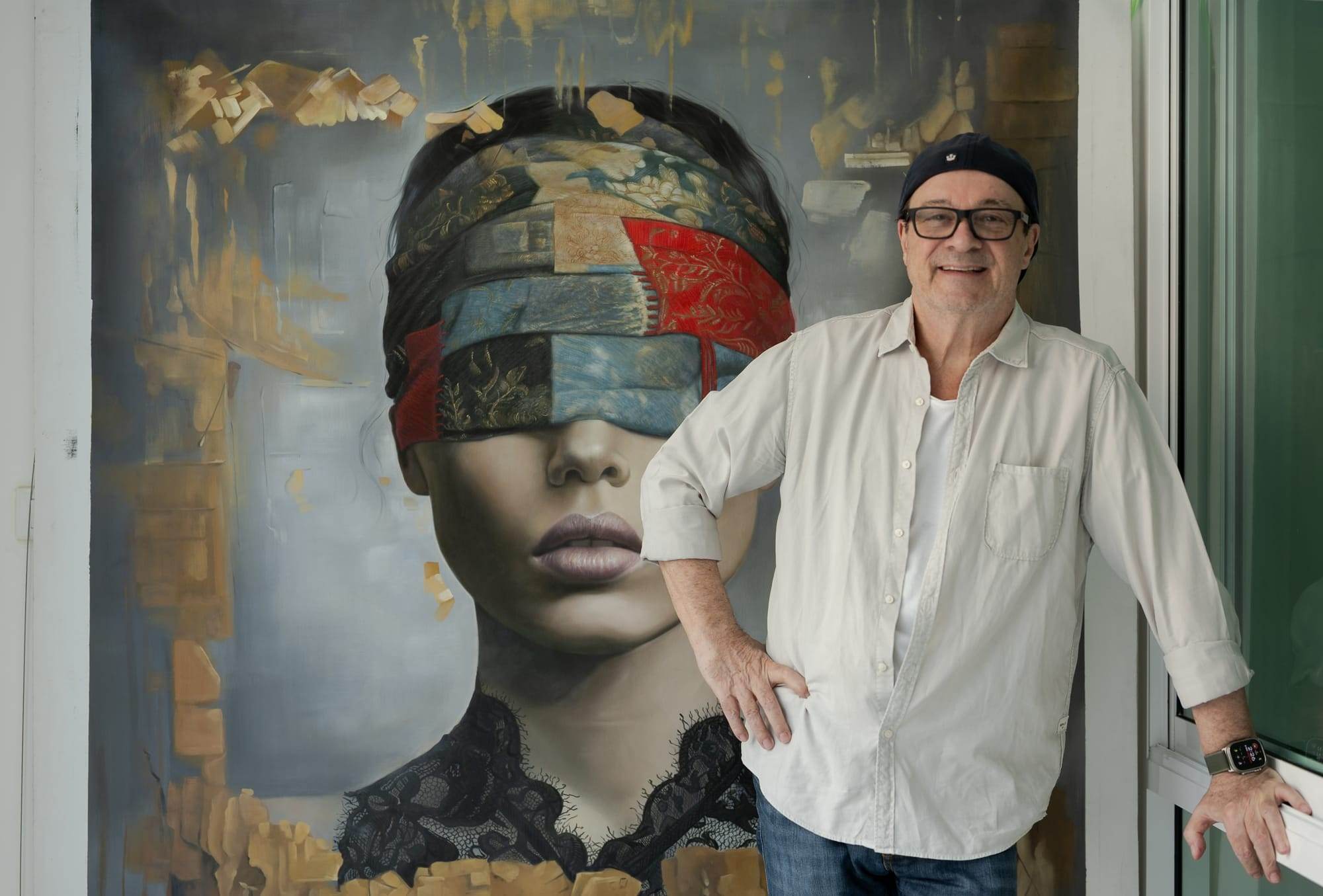 Jehan Legac posing in front of the exhibited painting Vision Within, featuring a large-scale contemporary portrait of a female figure with covered eyes.